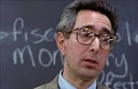 A teacher in glasses and a suit taking attendance with a deadpan expression