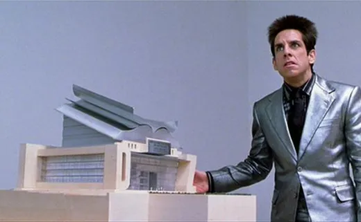 Derek Zoolander in a silver suit gesturing angrily at a small architectural model