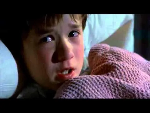 A frightened young boy lying under blankets, whispering
