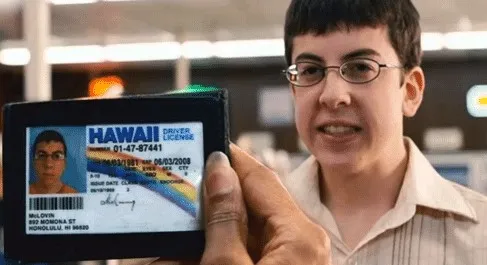 A nerdy teenager in glasses proudly holding up a Hawaii driver's licence