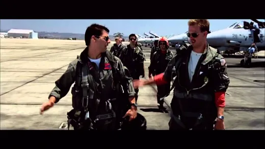 Two pilots in flight suits on an airfield, high-fiving