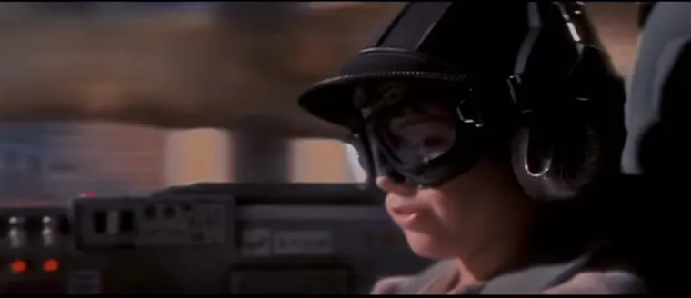 Young Anakin Skywalker in a podracing helmet and goggles, grinning in his cockpit