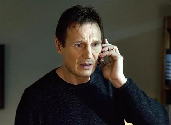 Liam Neeson holding a phone to his ear, with a serious expression