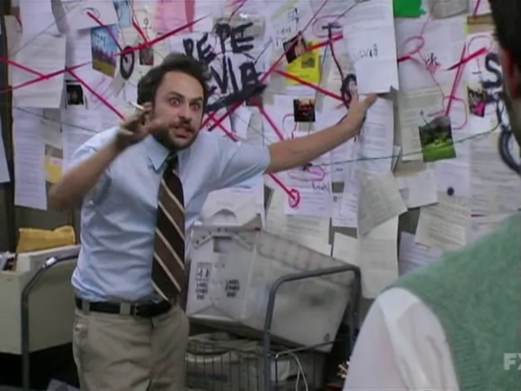 Charlie Kelly gesturing wildly in front of a wall covered in papers connected by string