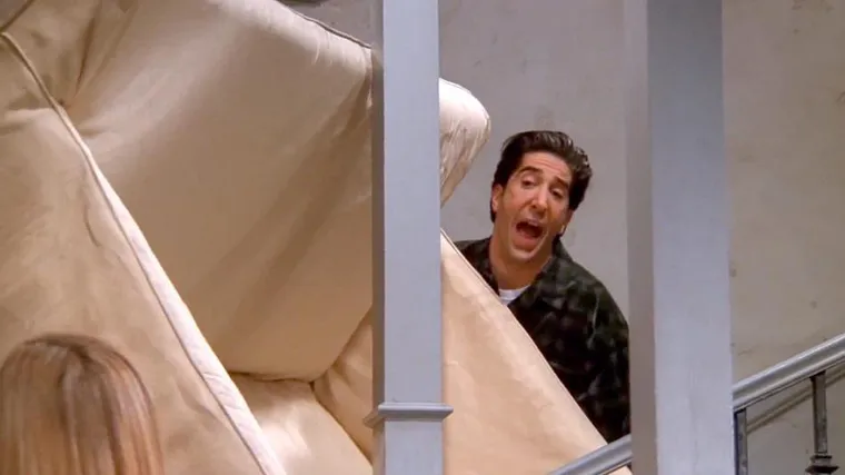 Ross shouting while carrying a sofa up a narrow staircase