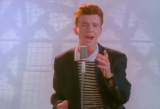 Rick Astley in a trench coat, dancing in front of a brick wall
