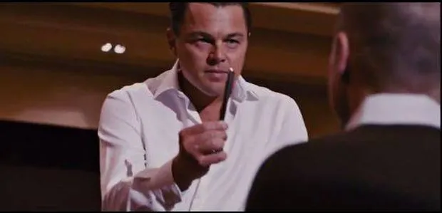 Leonardo DiCaprio as Jordan Belfort in a suit, holding out a pen