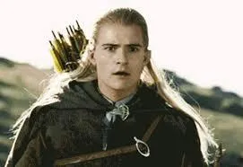 Legolas with long blond hair standing on a rocky hill, looking into the distance