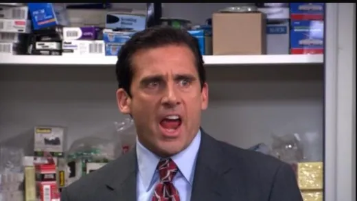 Michael Scott in a suit, standing in the office with a smug look