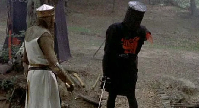 A knight in black armour with one arm missing, facing King Arthur in a forest