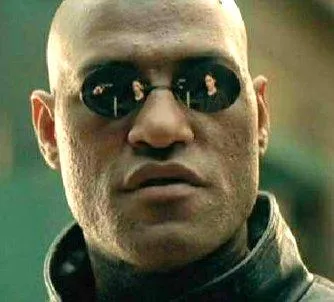 Morpheus in small round dark glasses and a leather coat, sitting in an armchair