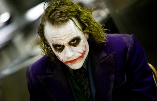 The Joker in smeared clown make-up and a purple coat, staring into the camera