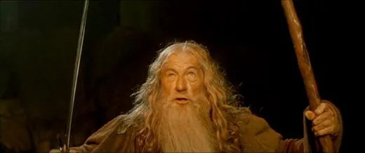 Gandalf in grey robes holding his staff and sword, shouting on a narrow bridge